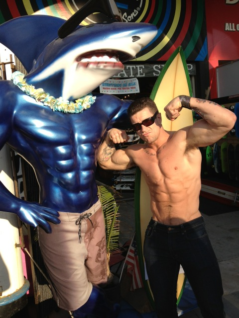 Trenton Ducati posing near a fake muscled shark on the boardwalk flexing his huge biceps and hard abs