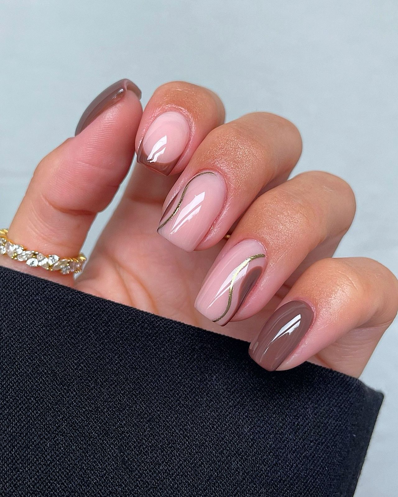 Close-up of a hand with glossy manicured nails in shades of pink and brown with delicate white designs.