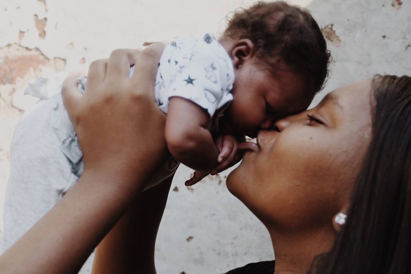 Photo of a mother lifting her baby in the air and kissing their nose.