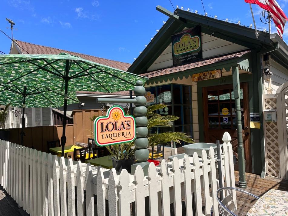 A small restaurant with a white picket fence and umbrella  AI-generated content may be incorrect.