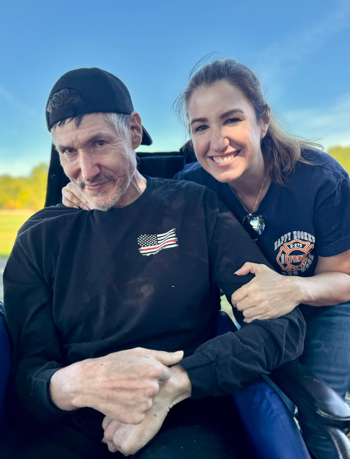 A smiling woman with her hand on the shoulders of a man in a wheelchair 