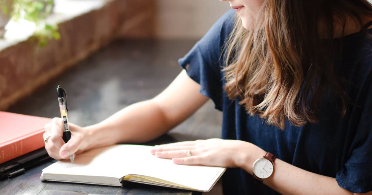 A woman diligently writing in her journal, surrounded by notes and an outline for inspiration in a serene setting.
