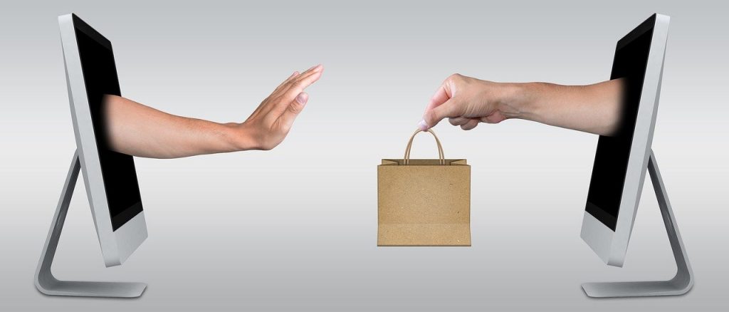 A pair of hands passing a shopping bag through two computer monitors. 