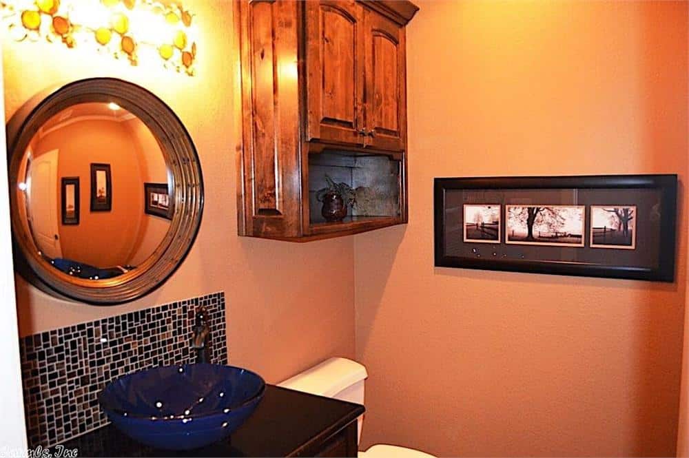 Powder room with peach walls, a hanging cabinet, and a vessel sink vanity topped with a round mirror.