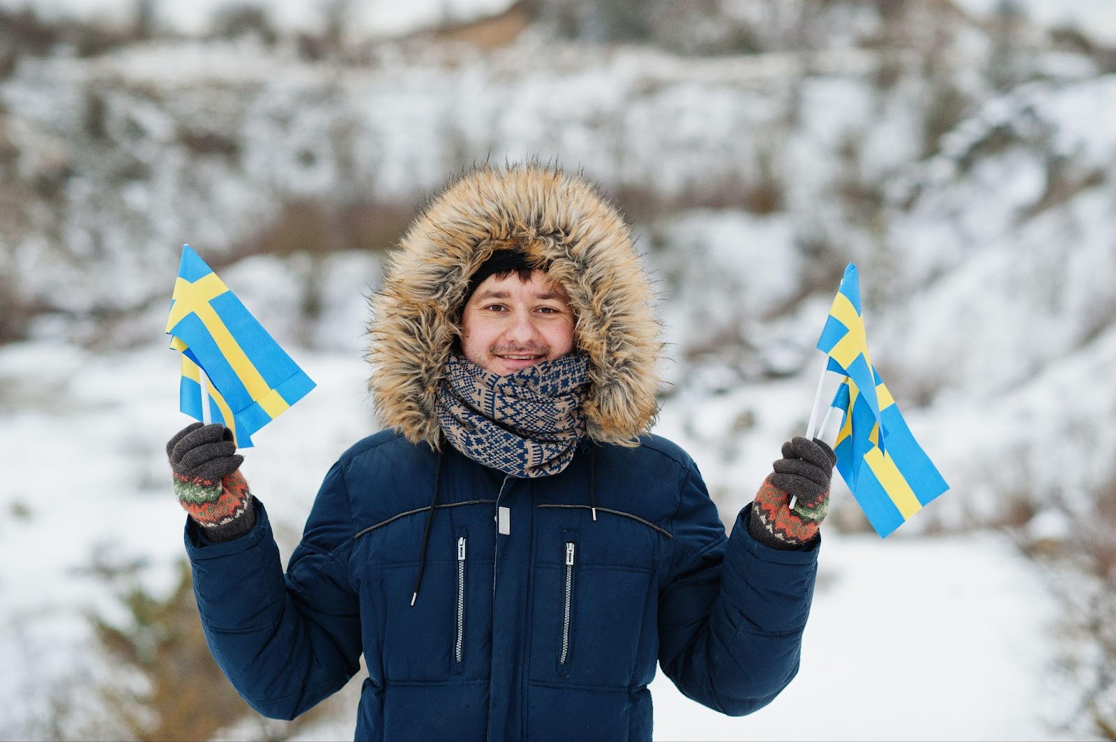 man in a blue coat in a snowy location holding flags