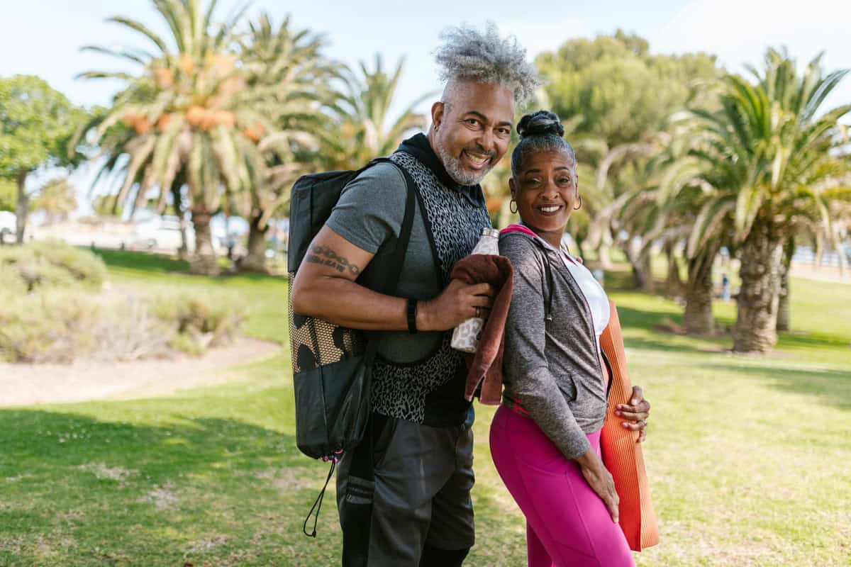 Foto de um homem e uma mulher a céu aberto num gramado o homem está com uma bolsa para tapete de yoga que facilita o transporte de acessórios de yoga.