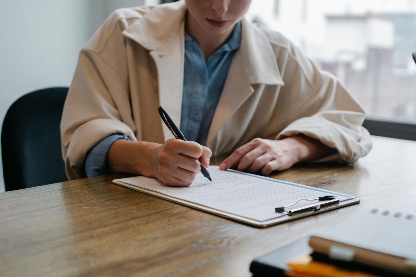 college female graduate sitting and writing cover letter, holding a pen in hand