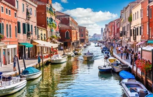 A canal with boats and buildings with Murano in the backgroundDescription automatically generated