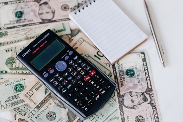 A calculator and a notepad resting on top of some American money.