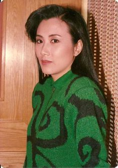 This contains an image of Liza Wang wearing a green and black sweater 