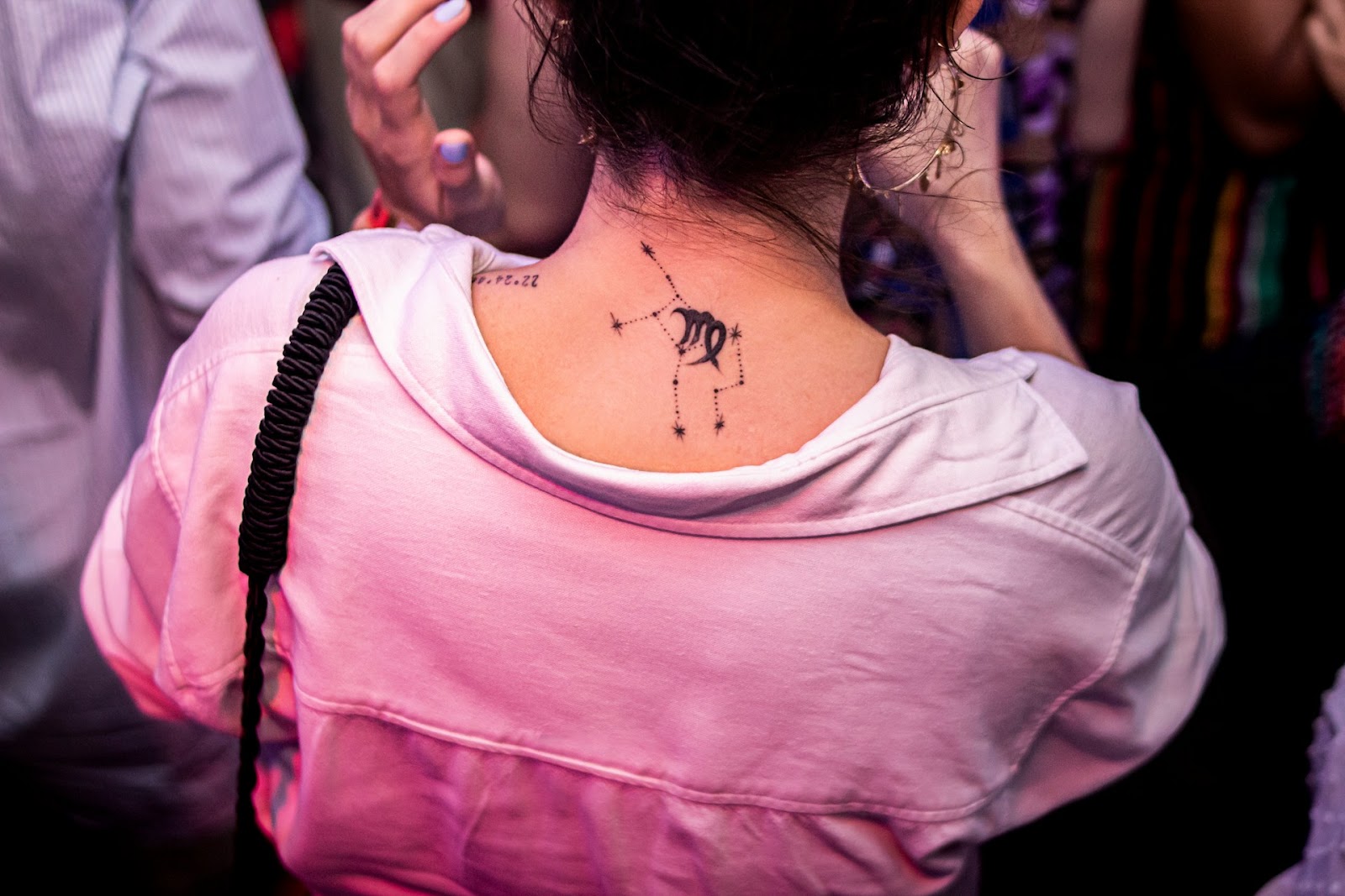 A person in a pink shirt with a constellation zodiac tattoo on her neck.