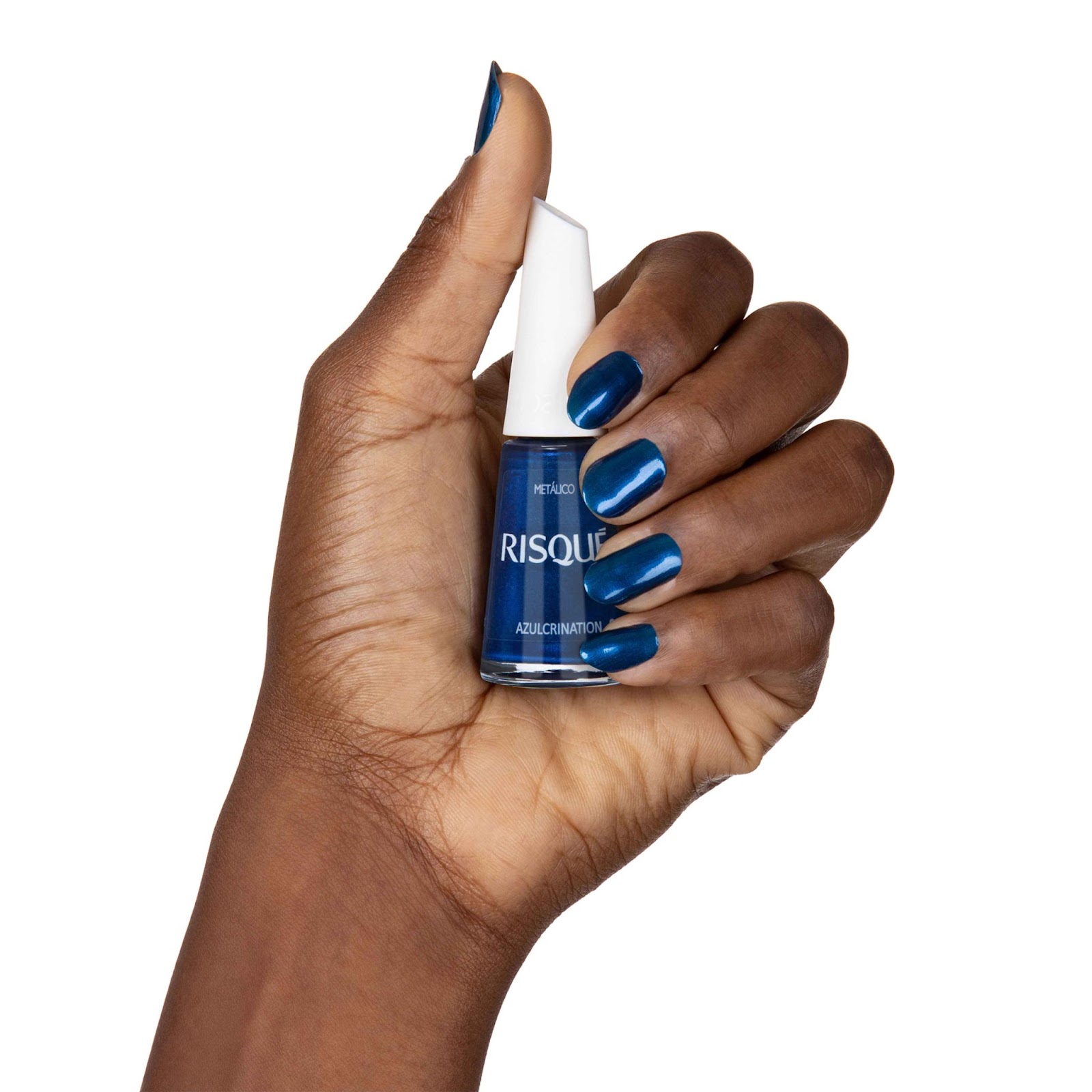 Uma mulher com as unhas pintadas de azul metálico segura o esmalte Risqué Azulcrination em uma das mãos.