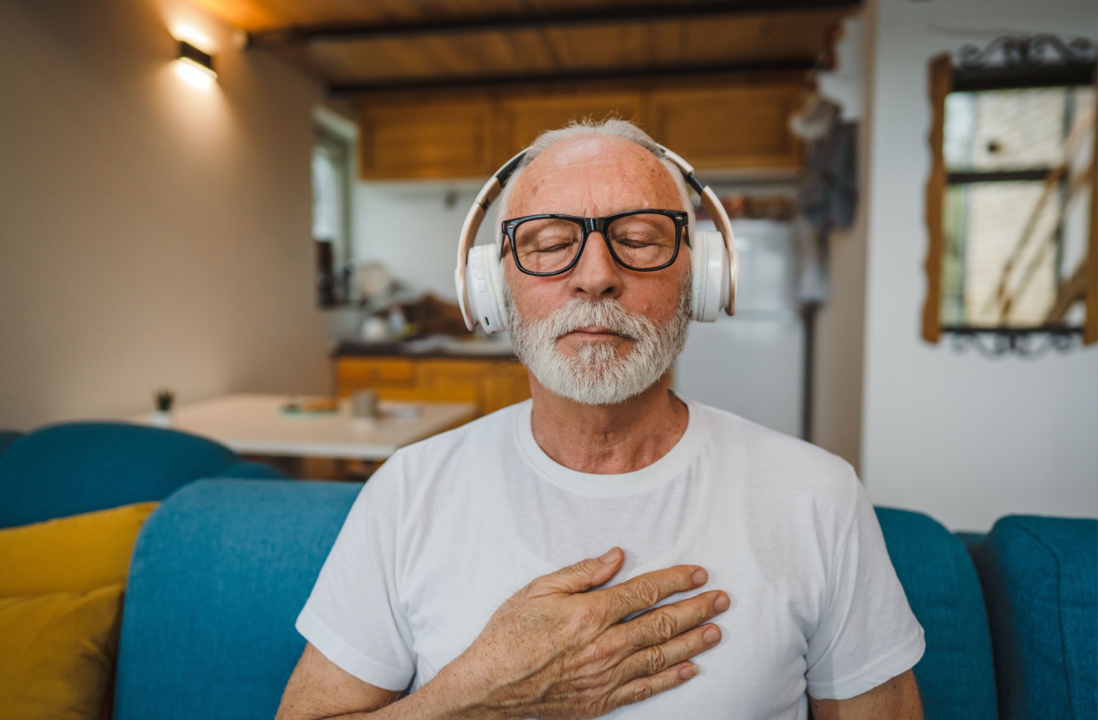 An older adult man closes his eyes while listening to a meditation program on headphones.