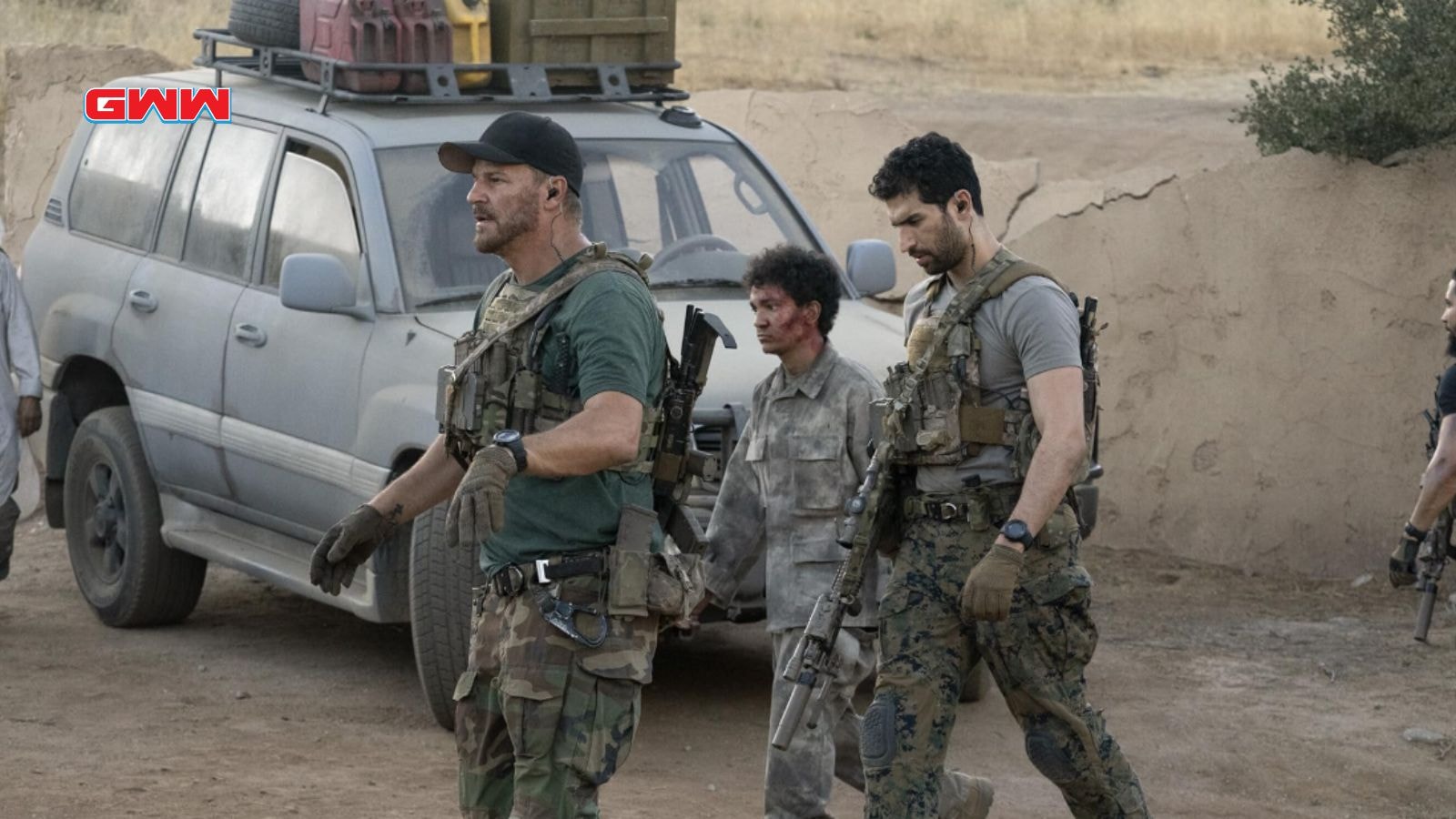 Jason and Omar escort a wounded man near an SUV in a desert.