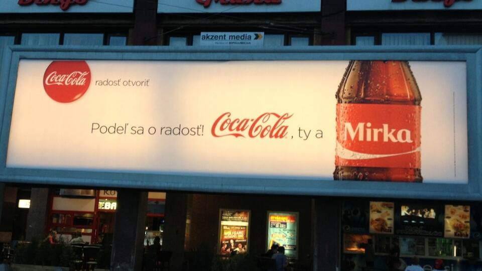 Billboard reklama značky Coca-Cola s textom „Podieľ sa o radosť! Coca-Cola, ty a Mirka.“ Na pravej strane je zobrazená fľaša Coca-Coly s personalizovaným menom „Mirka“ na etikete. Reklama je zameraná na zdieľanie radosti prostredníctvom personalizovaných fliaš.