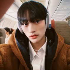 This contain an image of TRCNG's Taesonwith headphones on his ears sitting in an airplane looking at the camera