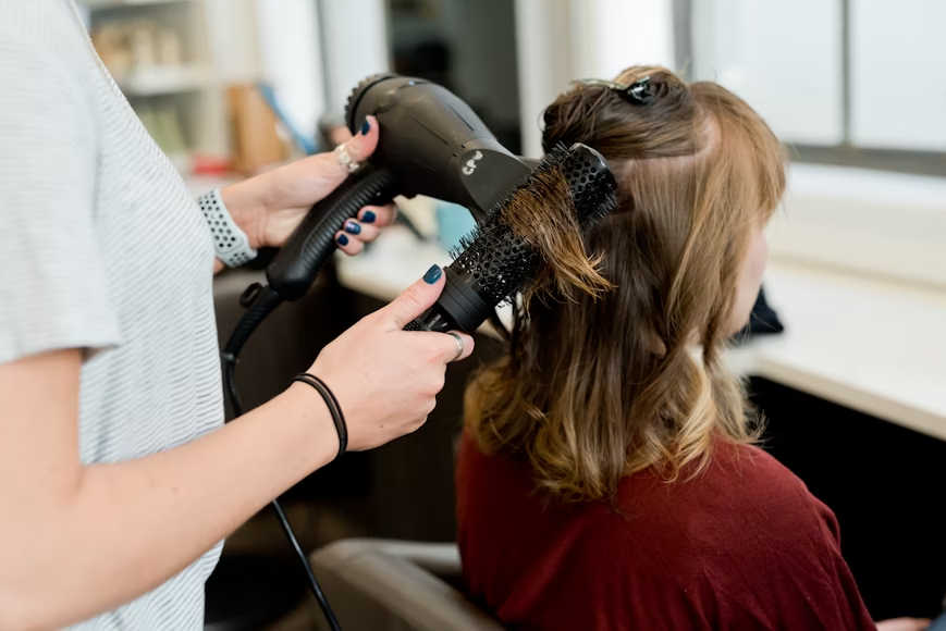 Hair stylist blow drying client's hair and combing it