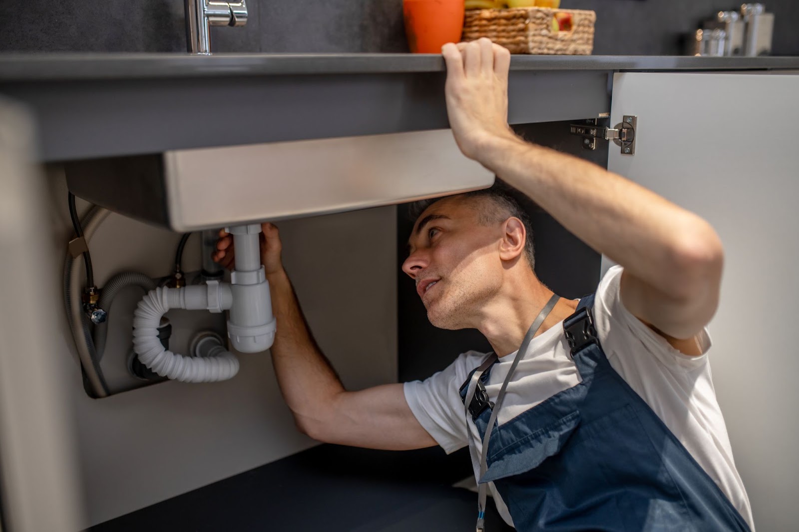 A local plumber carefully inspects the bottom of a sink and pipe for issues.