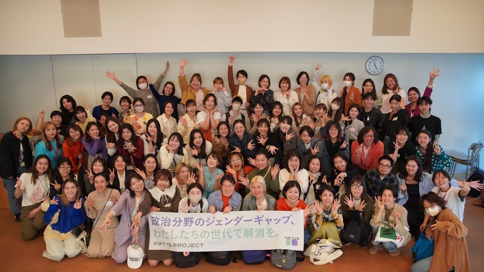 FIFTYS PROJECTのメンバーの集合写真。「政治分野のジェンダーギャップ、わたしたちの世代で解消を」と書かれたバナーを持っている。