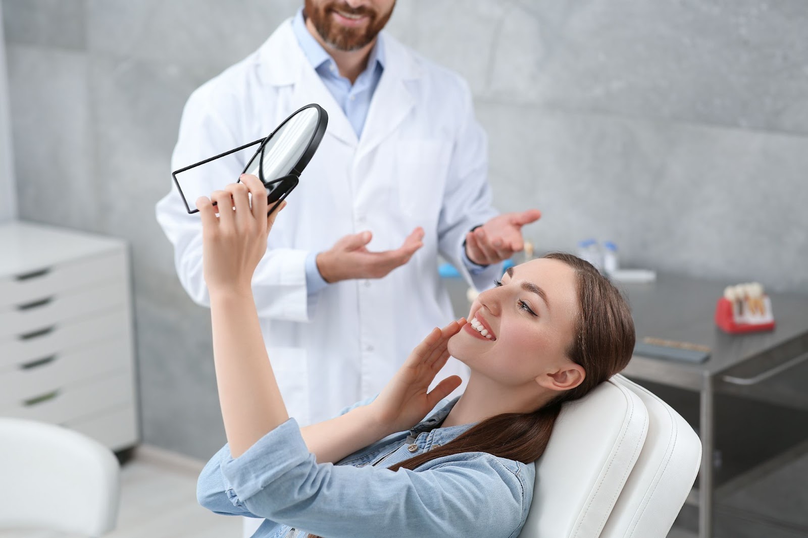 A young woman smiling while admiring her new dental implant in a handheld mirror.