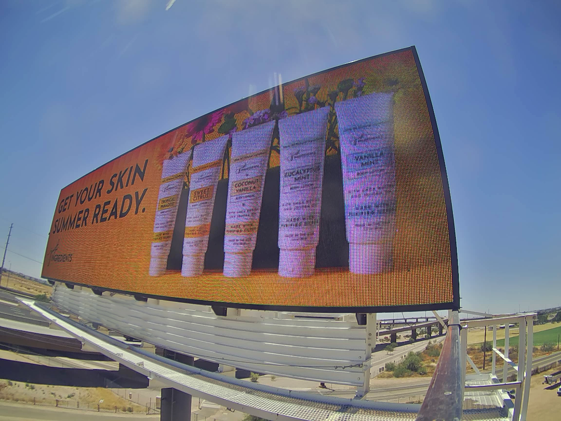 LED billboard advertising skin moisturizer with 5 small bottles of the product with various colors and flowers in that background that reads "Get your skin ready for summer".