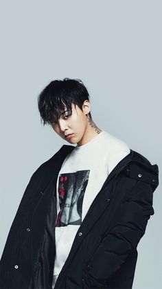 This contains an image of  G-dragon with black hair and piercings standing in front of a gray background