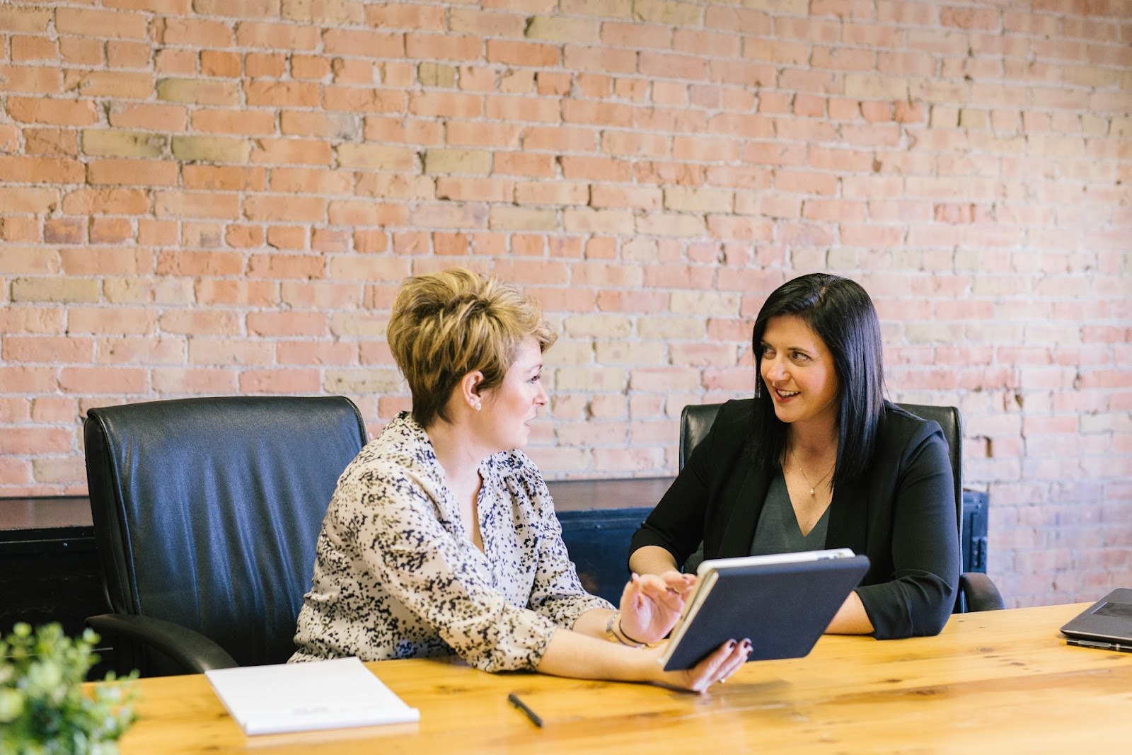 Two women chatting and sharing ideas at a table while looking at a tablet together.