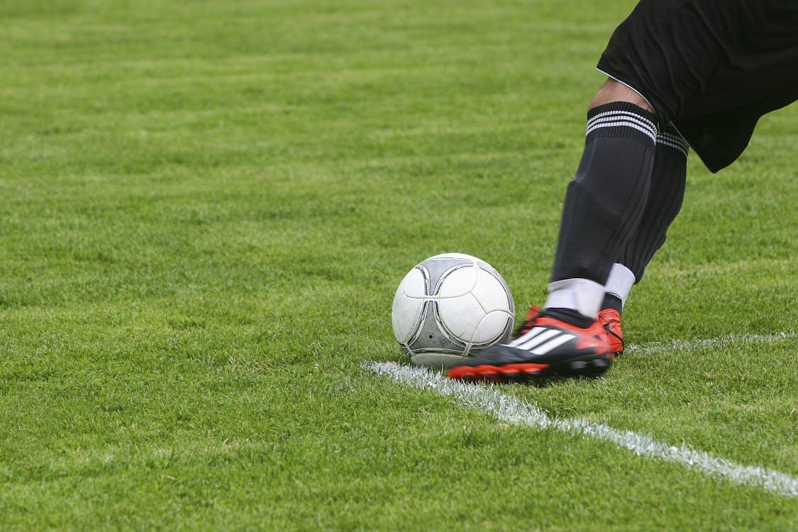 Free Soccer Player Kicking White Gray Soccer Ball on Green Grass Field Stock Photo