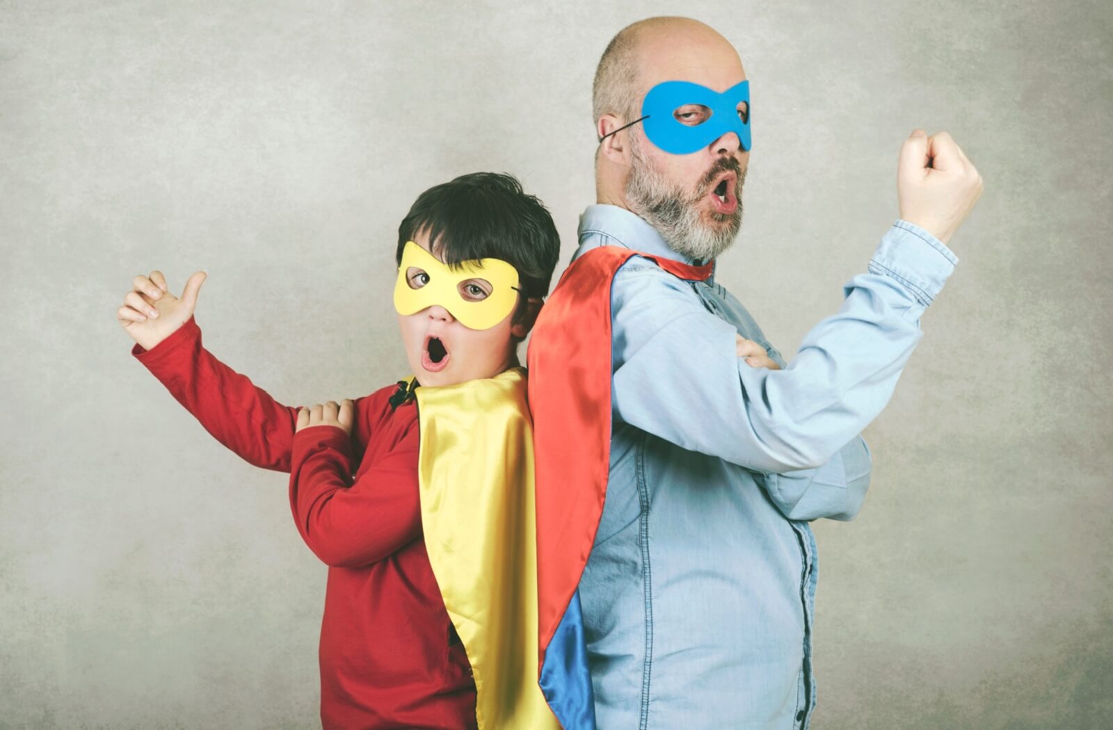 A child and their grandparent stand back to back in superhero costumes