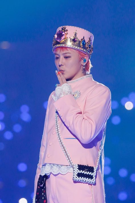 This contain BIGBANG G-Dragon  in a pink outfit with a crown on her head and hands to her face