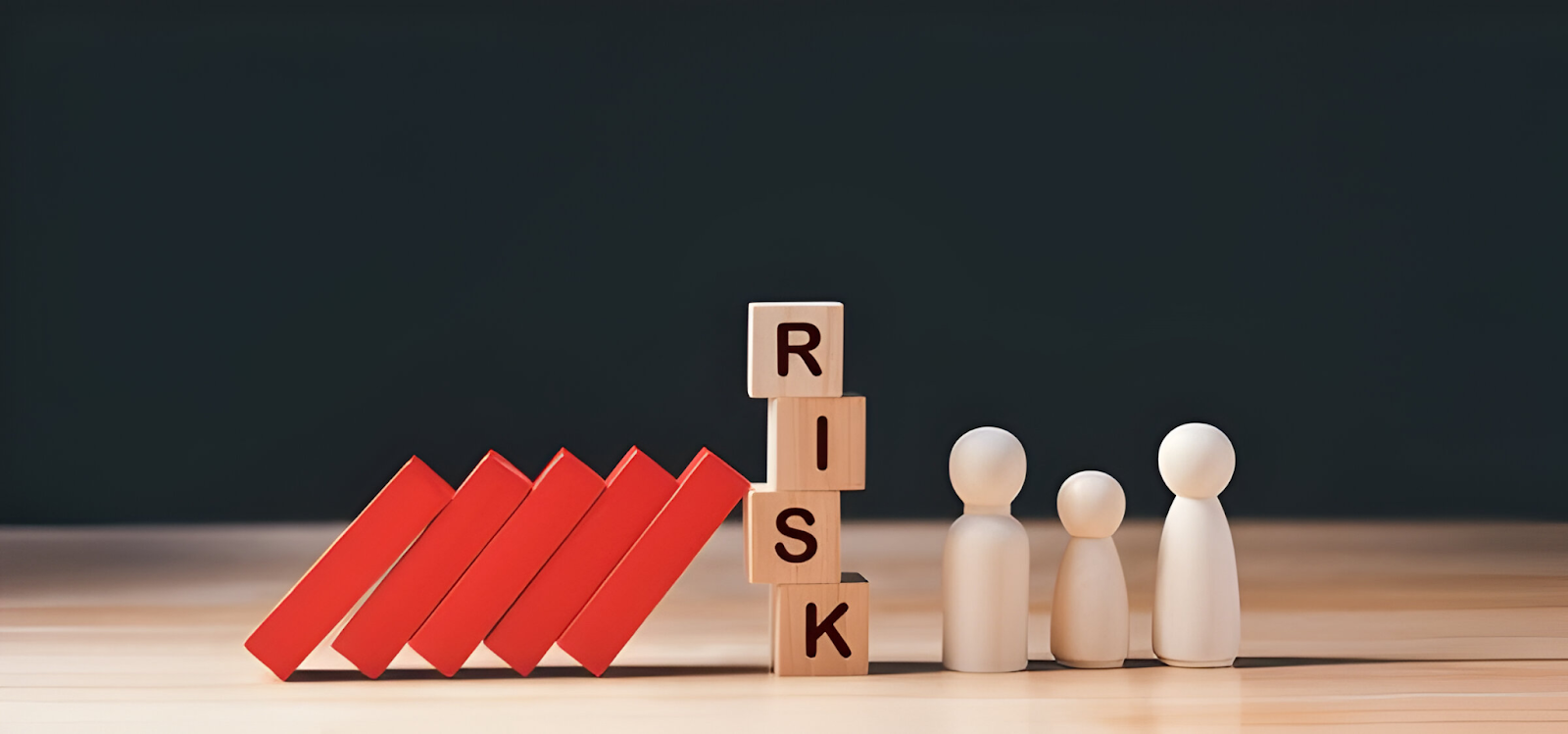 Wooden blocks spelling 'RISK' stacked vertically, preventing a row of falling red dominoes from reaching wooden figures, symbolizing the mitigation of financial risks.