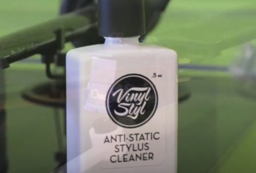 A bottle of Vinyl Styl Anti-Static Stylus Cleaner placed in front of a turntable. 