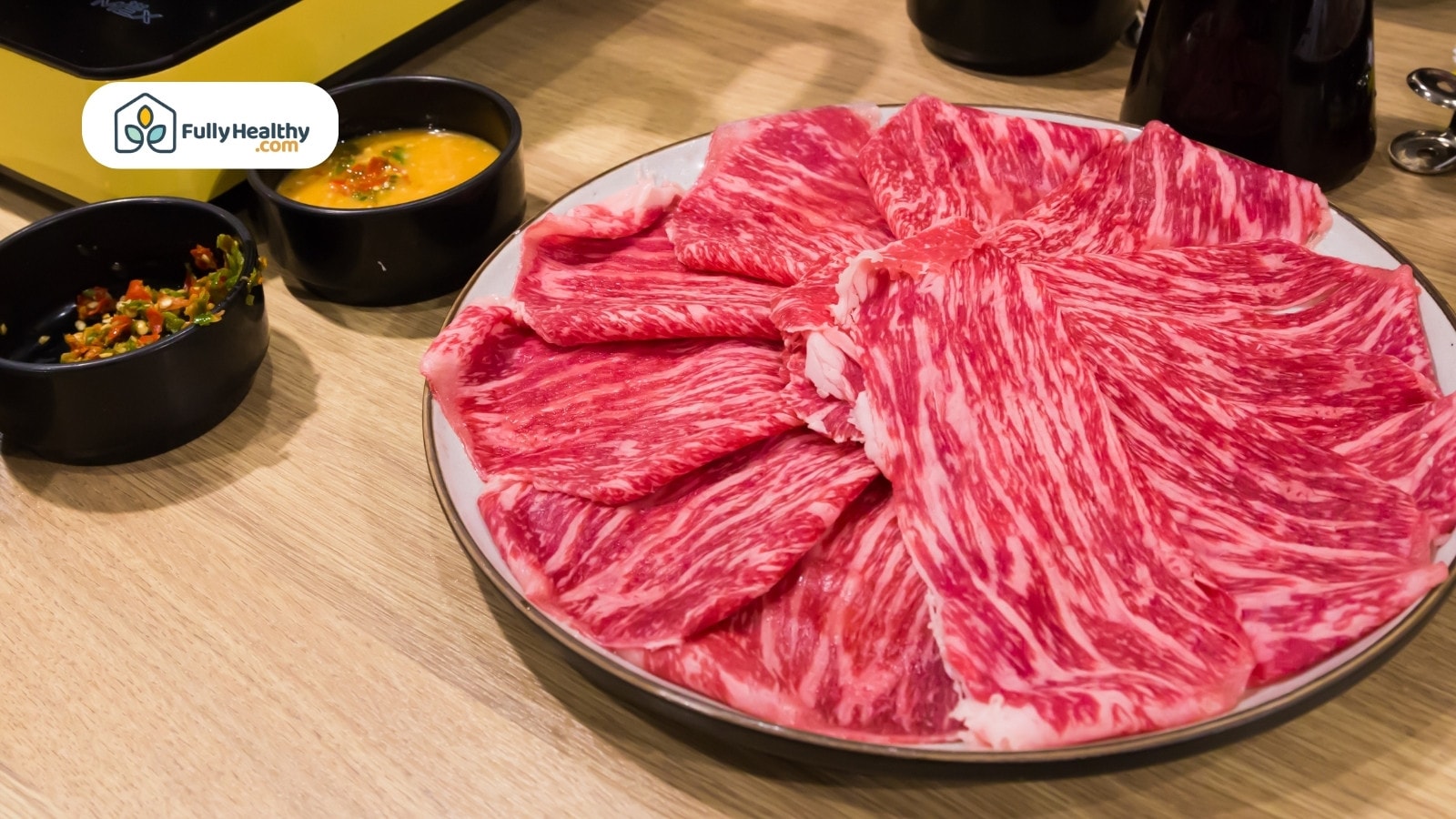 Thinly sliced marbled beef arranged on plate beside dipping sauces
