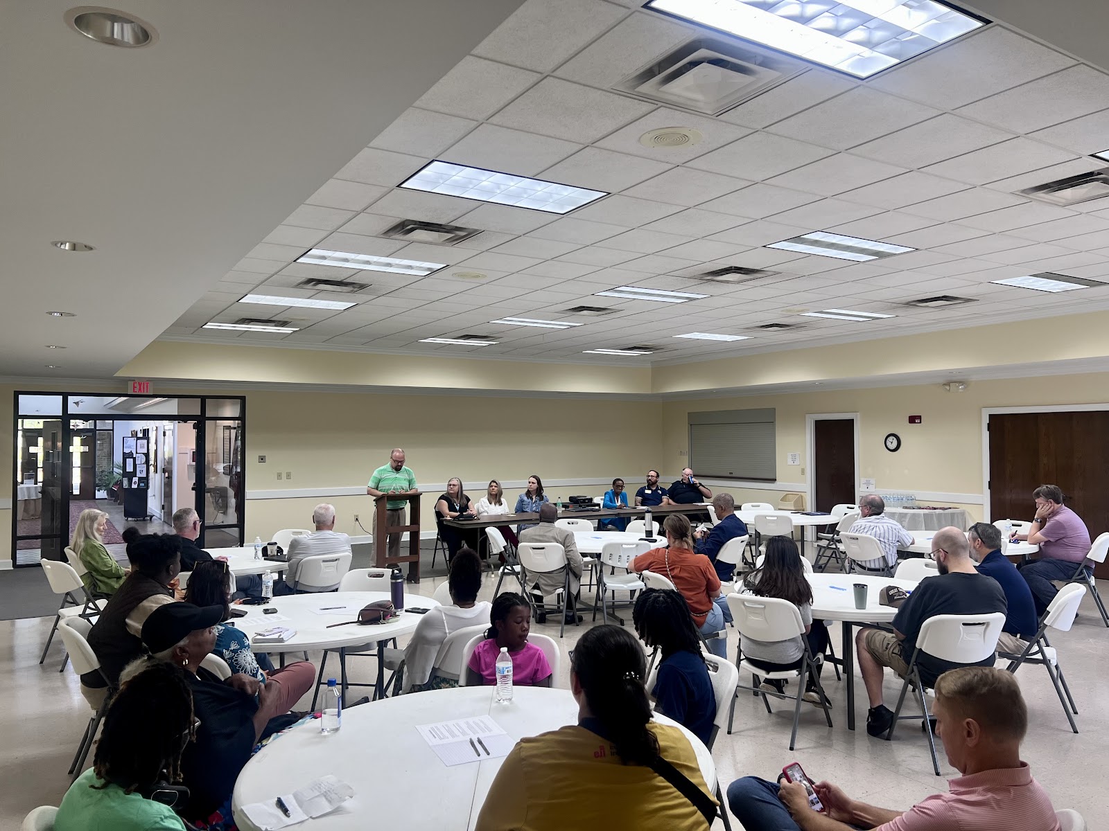A picture of from the back of the room, showing the tables full of community members.