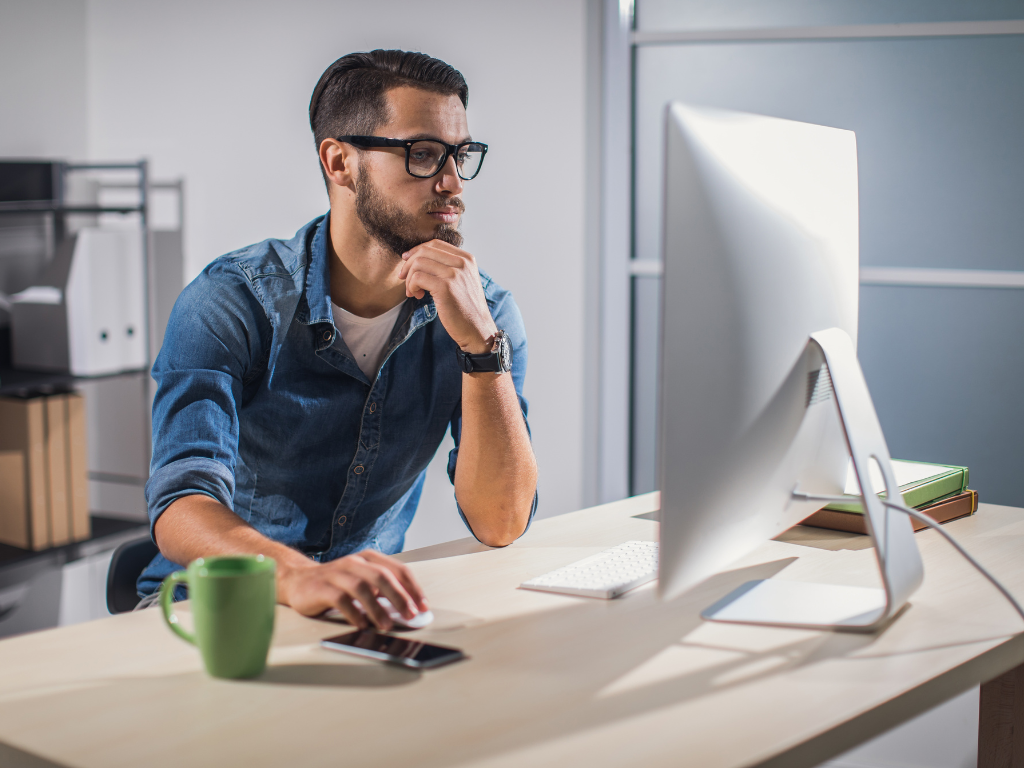 a man working on his laptop with a cup of tea placed besides