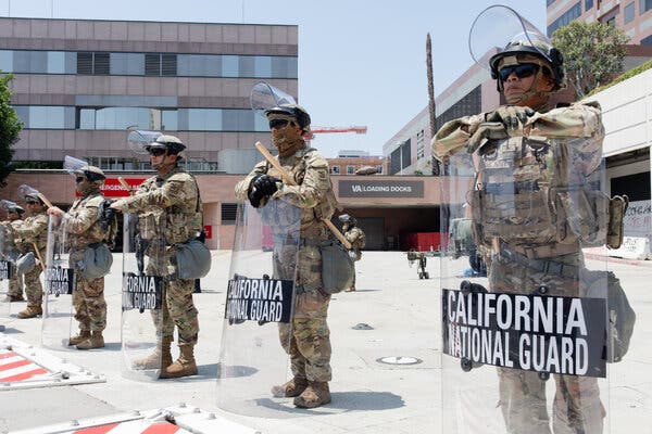 Soldiers in uniform hold clear shields with the words “California National Guard” on them.