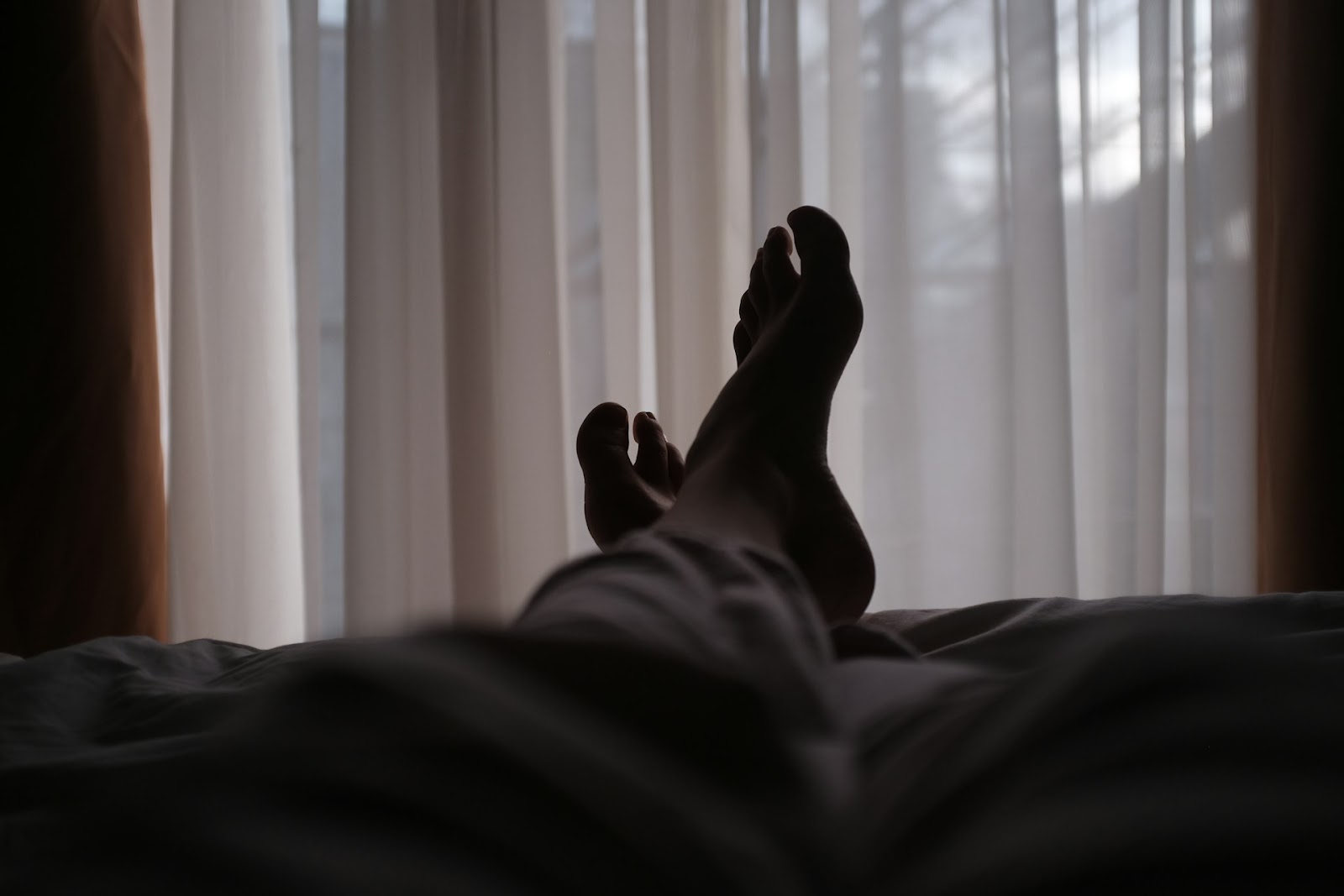 Someone sleeping by a window with their feet crossed by the curtains