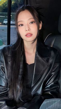 This contains an image of  BLACKPINK Jennie sitting in the back seat of a car wearing a leather jacket and black pants