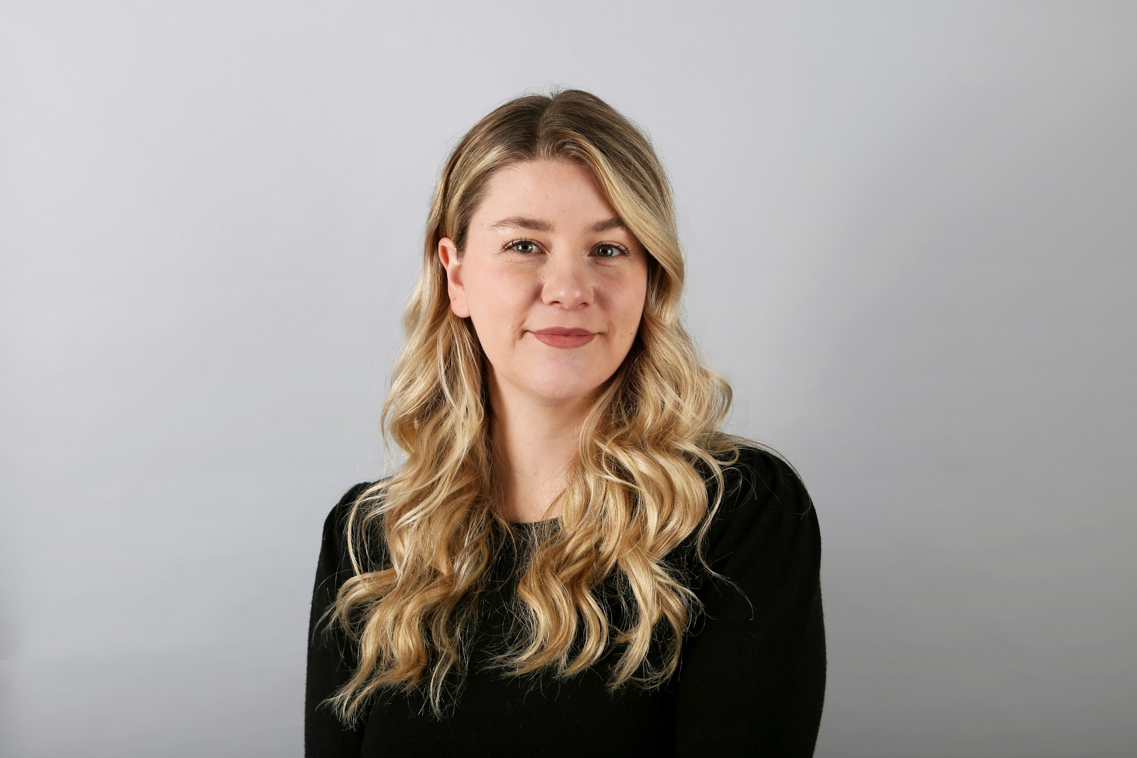 A blonde woman wearing black in front of a neutral background posing for a headshot