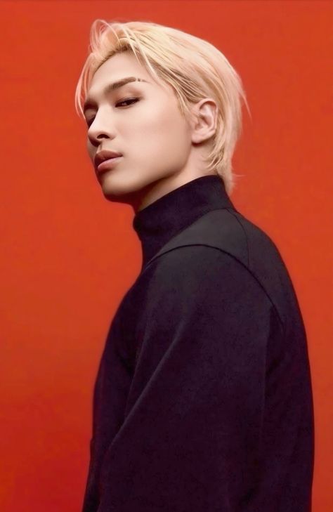 This contain BIGBANG's Taeyang with blonde hair wearing a black shirt and looking off to the side while standing in front of a red wall