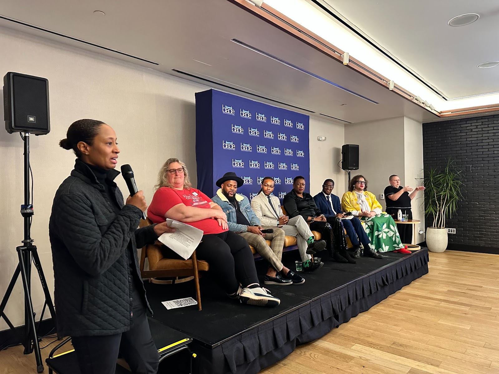 A woman holds a microphone next to a seated panel. 