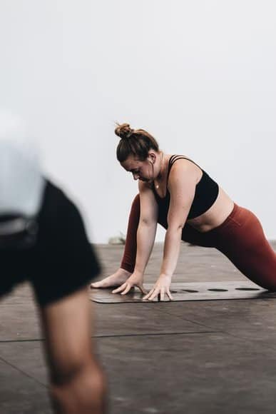 An individual performing a physical exercise on a yoga mat. The person is wearing a black tank top and maroon leggings. 