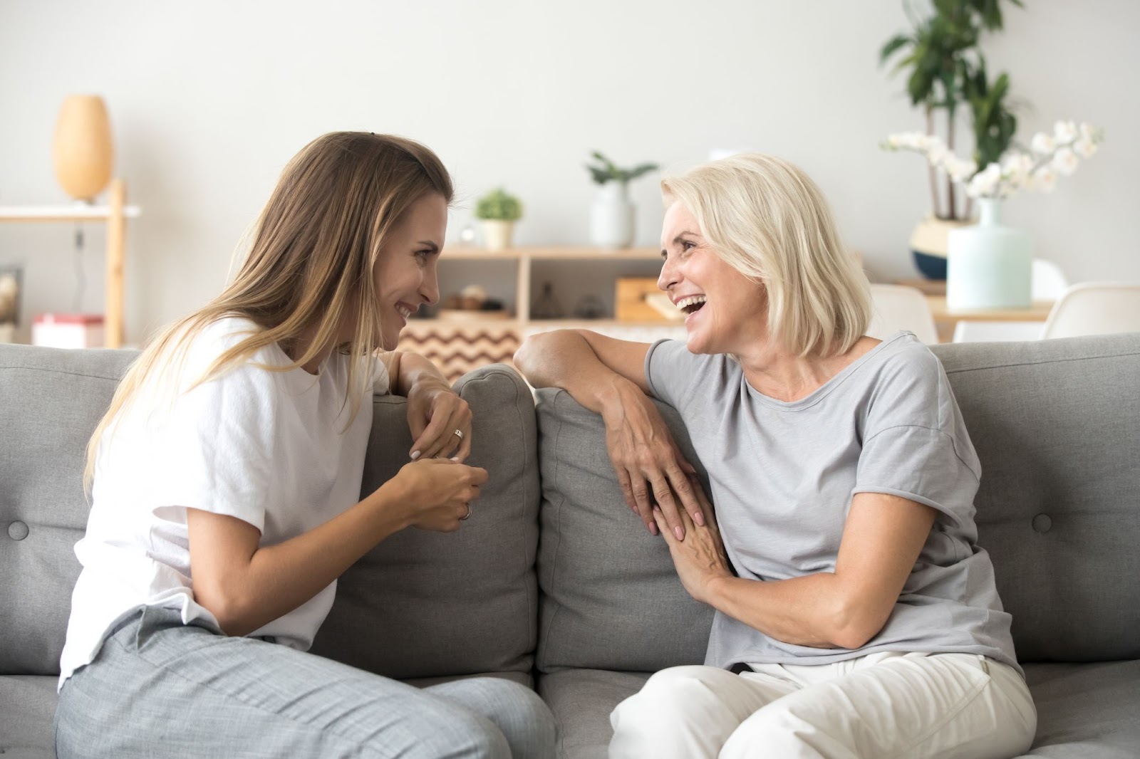 An adult woman and her older mother talking on a couch and laughing together.