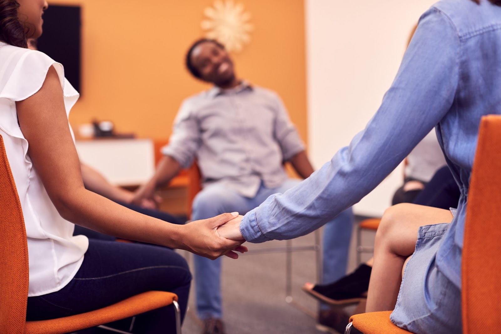 People holding hands while sitting in chairs placed in a circle.