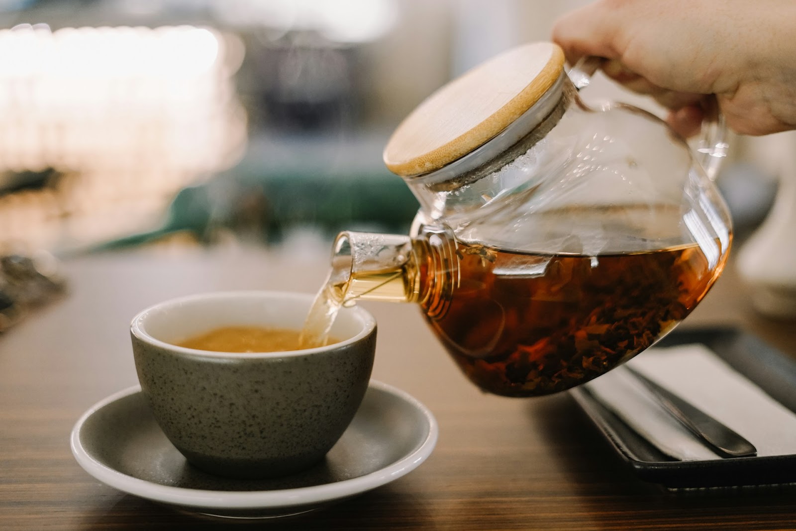 Someone pouring tea from a glass teapot into a mug