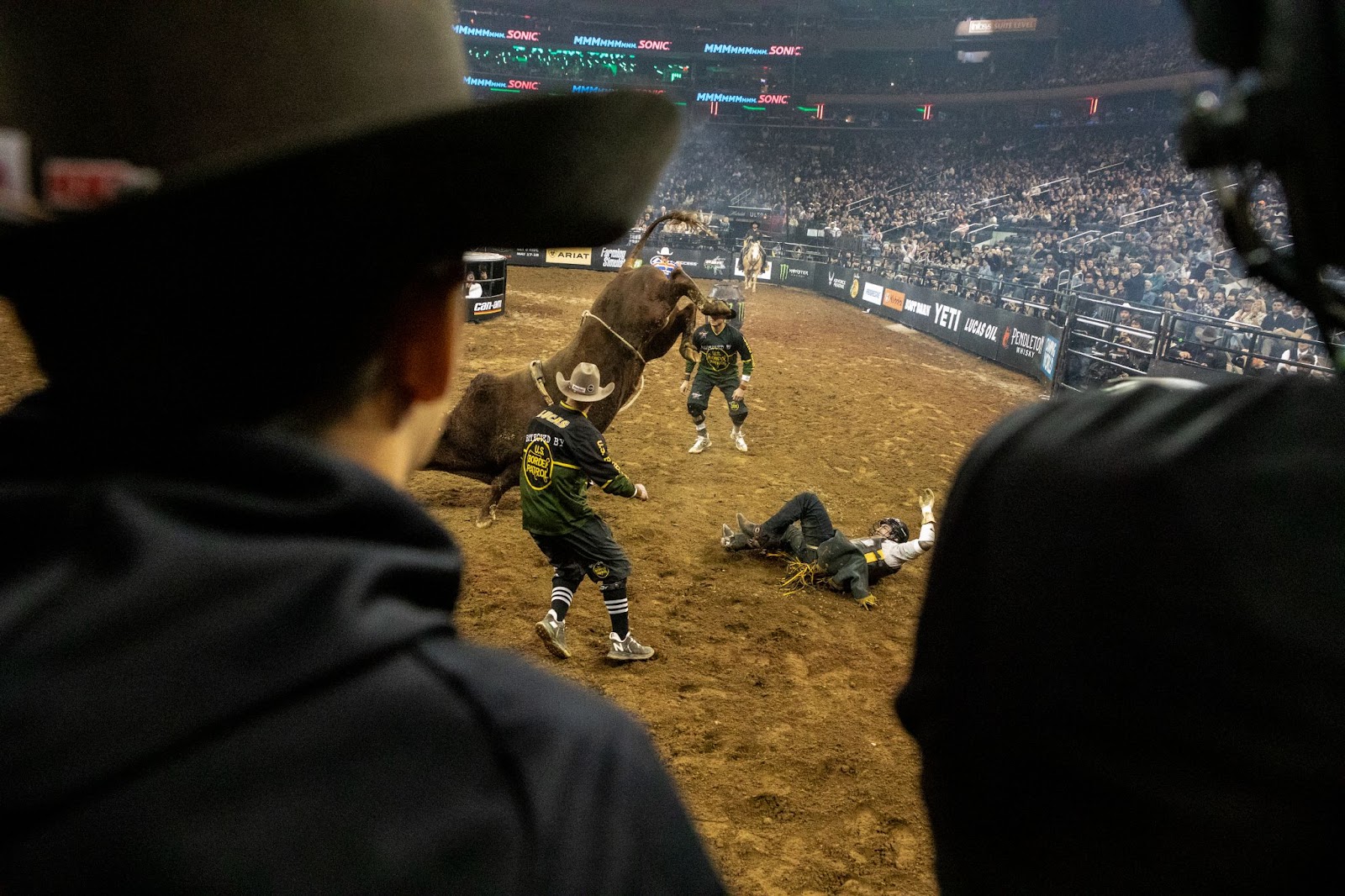 Rider is thrown from brown bull. Bullfighters surround him to assist.