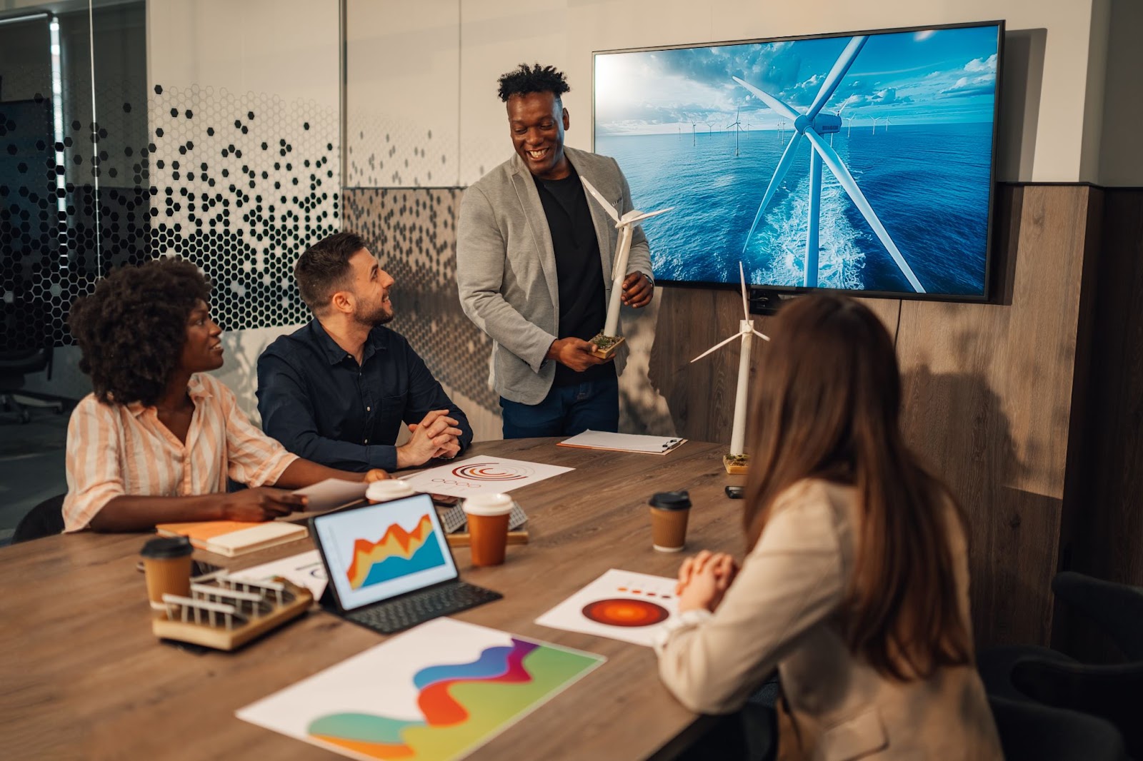 An ecology expert presenting a wind turbine model to investors during a meeting on sustainable business operations in an office.