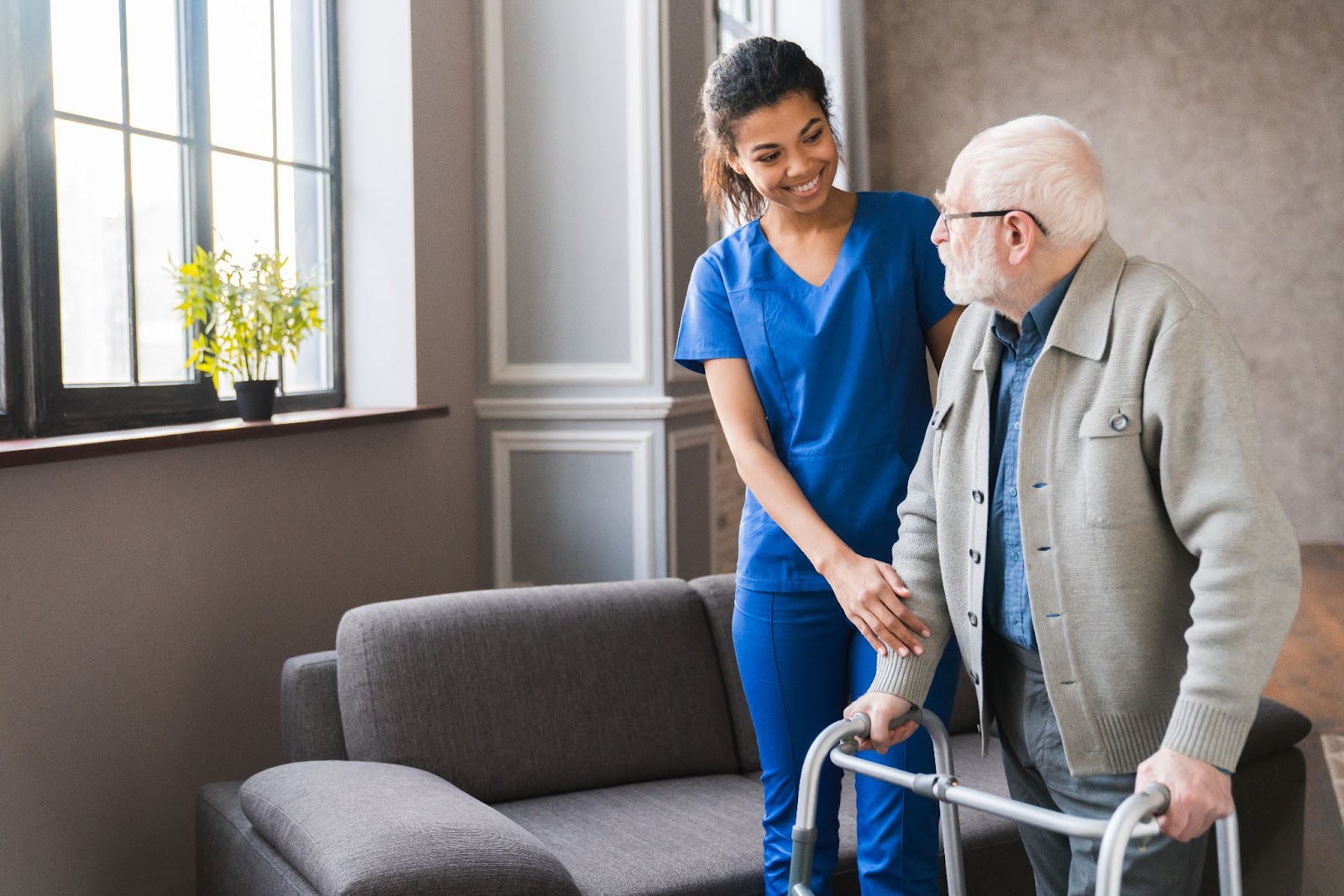 A young caregiver smiling at a senior man in assisted living as she helps him with his walker.