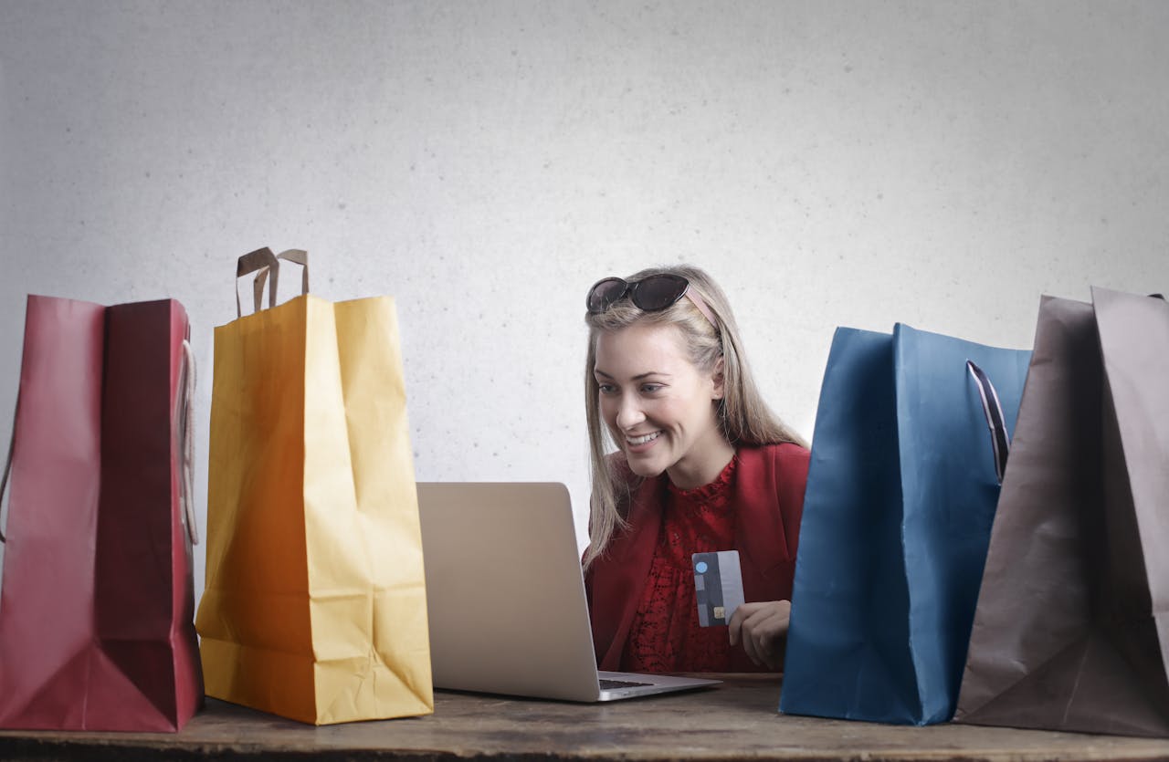 A woman holding a credit card, smiling while shopping online surrounded by colorful shopping bags, symbolizing ecommerce business growth.