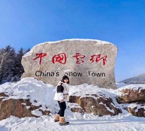 A person standing in front of a large rock with snow  Description automatically generated